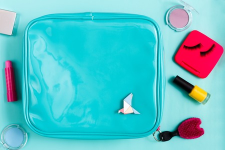 Beauty products. Cosmetic bag with  essentials - eyelashes, eyeshadow, lipstick and nail polish on blue background, flat lay, top viewの写真素材