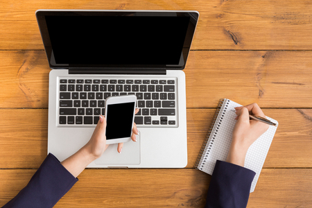 Top view table of business woman checking schedule with mobile phone. Freelancer working with portable computer while sitting at wooden desk at coffee shopの写真素材