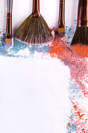 Make up and female cosmetics background. Makeup brushes vertical border with blush and eyeshadow of pink, blue and coral tones sprinkled on white.の写真素材