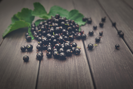 Fresh black currants on rustic wood background. Natural organic berries with green leaves scattered on weathered grey wooden table, dark filterの写真素材