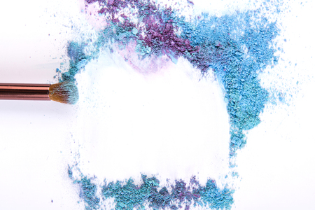 Makeup brush background with eyeshadow of blue and violet tones sprinkled on white. Make up and female cosmetics backgroundの写真素材