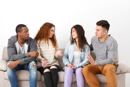 Education and co-working. Diverse students discuss question, sitting on couch at home interior, studio shotの写真素材