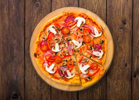 Italian pizza top view with mushrooms and pepperoni - thin pastry crust isolated at wooden background, with piece cut offの写真素材