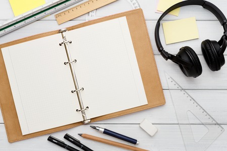 Education and work concept, top view shot of workplace. Stationery supplies - blank notepad and headphones on white wooden desktop, flat lay, copy space, mockupの写真素材