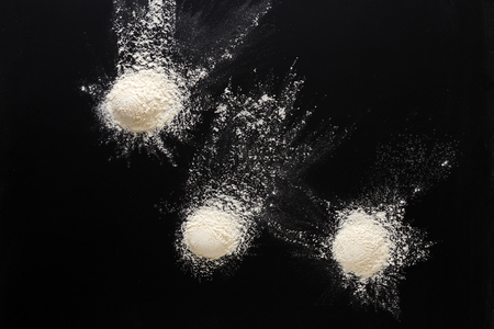Sprinkled wheat flour splash spots on black background. Top view on blackboard. Baking concept, cooking dough or pastry.の写真素材