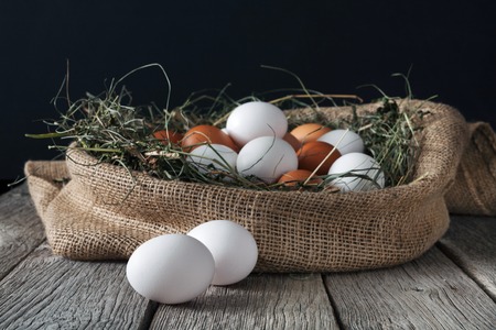 Fresh brown and white eggs in burlap sack at rustic wood isolated on black backgroundの写真素材
