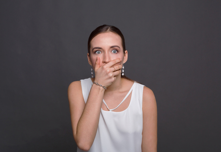 Shocking news. Scared woman covering mouth with hands while posing to camera on gray studio background.の写真素材