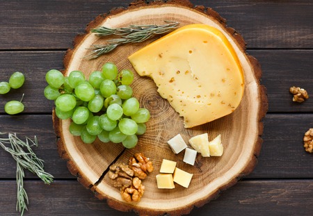 Cheese platter, gouda herb on natural wood disc with grapes and nuts, still life, top viewの写真素材
