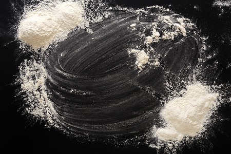 Baking class or recipe concept on black background, sprinkled wheat flour with free text copy space. Top view on blackboard or table. Cooking dough or pastry.の写真素材