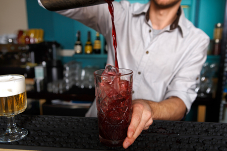 Barman in bar interior pouring red alcohol to cocktail drink from shaker. Professional bartender at work in night club. Service industry occupation. Vertical imageの写真素材