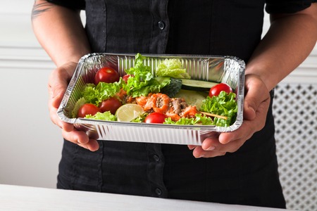 Healthy lunch at workplace in the office. Salad plate with salmon in female hands. Snack at break timeの写真素材