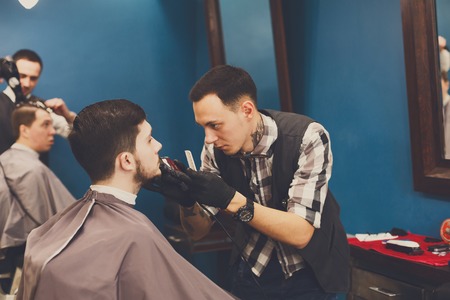Barber styling beard with trimmer at barbershop, closeup. Barbershop for menの写真素材