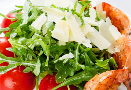 Restaurant healthy food, salad, arugula with shrimps and cherry tomatoes, covered with parmesan, closeup at white plateの写真素材