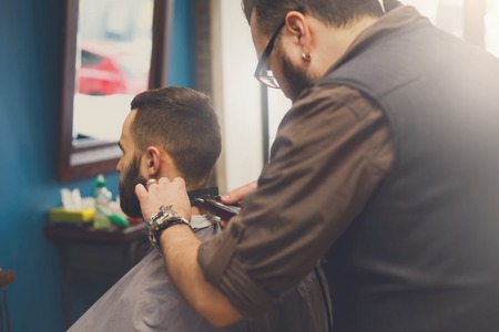 Barber make beard haircut with trimmer hair clipper in barbershop, closeup of clients head. Hairstyle in male hair salonの写真素材