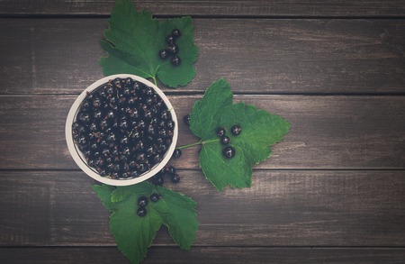 Fresh black currants bowl top view on rustic wood background. Natural organic berries with green leaves scattered on weathered grey wooden table, dark filterの写真素材