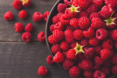 Raspberries bowl on rustic wood background, top view closeup. Organic berries with peduncles and green leaves on wooden tableの写真素材