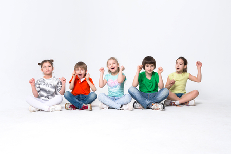 Happy kids. Group of children sit on floor at studio, posing to camera on white isolated background, copy spaceの写真素材