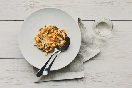 Italian restaurant food top view, carbonara pasta with bacon, egg yolk and parmesan decorated with basil on white round plate.の写真素材