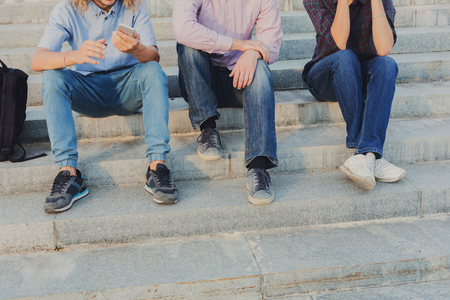 Group of people with gadgets outdoor, copy space. Company of three unrecognizable friends have rest on stairs in street. Modern technologies and communication problem conceptの写真素材
