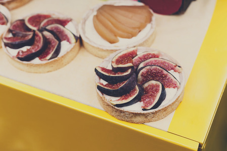 Fruit and berry tarts dessert tray assorted. Closeup of beautiful delicious pastry sweets with fresh natural figs. French Bakery catering. Filtered, shallow depth of fieldの写真素材