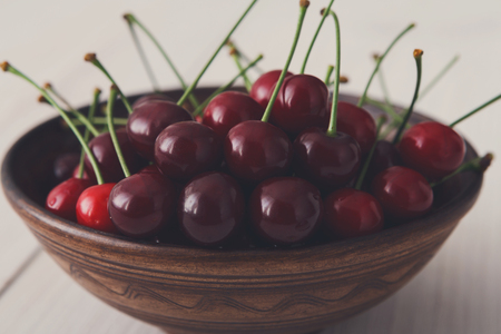 Sweet fresh cherries in bowl closeup at wooden background. Juicy fruits on white rustic wood table. Healthy organic food.の写真素材