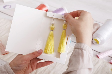 Handmade earrings packing, home workshop. Woman artisan put tassel jewelryinto original boxes, top view. Art, hobby, handicraft conceptの写真素材