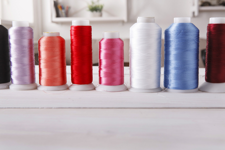 Colorful thread spools on wooden table close up. Sewing string, copy space for text. Art, handicraft...