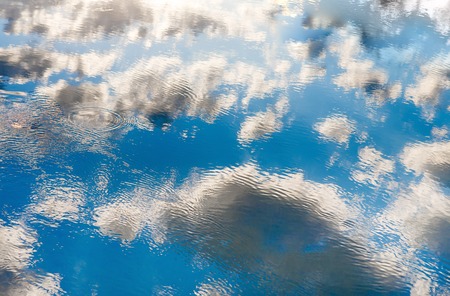 Blue cloudy sky reflection in rippled water. Sunny and windy weather. Nature background
