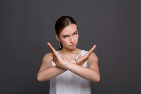 Woman making stop sign with crossed hands. Serious girl denying, refusing any action, looking at camera, dark backgroundの写真素材