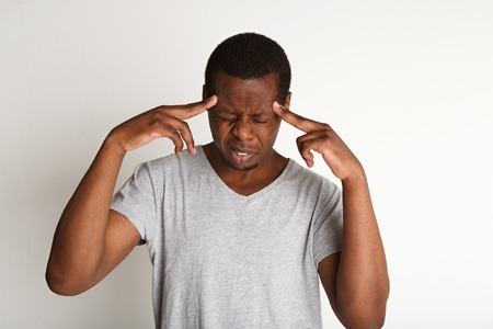 Headache. Concentrated pensive black man thinking about something, holding fingers on temple, white studio backgroundの写真素材