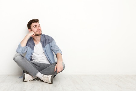 Pensive young man sitting on floor and looking upwards. Handsome relaxed guy dreaming about...