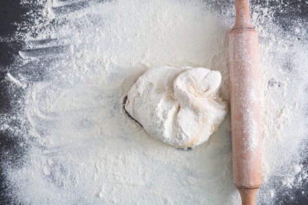 Homemade bakery. Top view of raw dough on black table covered with flour, rolling pin on dark background, closeup, copy spaceの写真素材