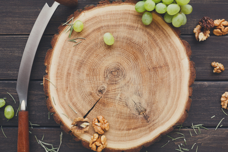 Grapes and nuts on natural wood disc on rustic background, two-handed knife for cheese aside, still life, top viewの写真素材