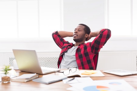 Relaxed black businessman in casual with laptop in modern white office interior.の写真素材