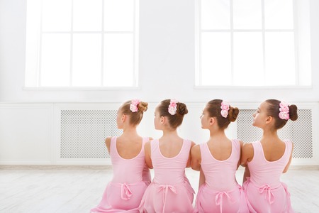 Little ballerinas in ballet studio. Group of girls having break in practice, sitting on floor, back view. Classical dance schoolの写真素材