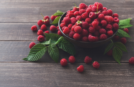 Raspberries bowl on rustic wood background, copy space. Organic berries with peduncles and green leaves on wooden tableの写真素材