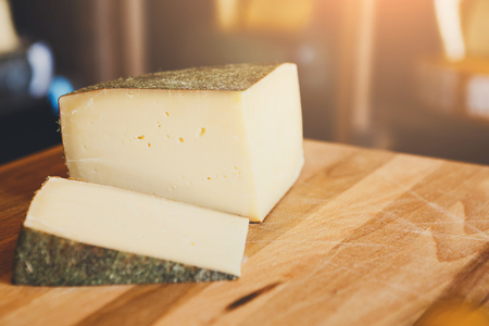 Hard cheese pieces on wooden table at grocery shop background. Gruyere in herbs shell, closeup