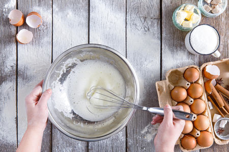 Overhead of baker hands whisking egg-white, copy space. Cooking ingredients for pastry on sprinkled with floor rustic wood, culinary classes or recipe concept.の写真素材