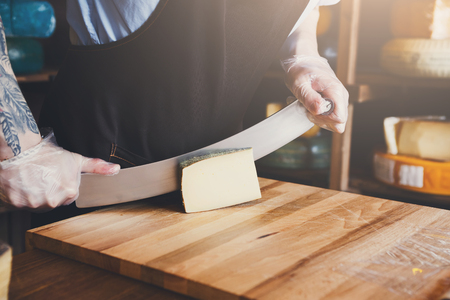Cutting hard cheese, pecorino cheese in grocery shop, closeupの写真素材