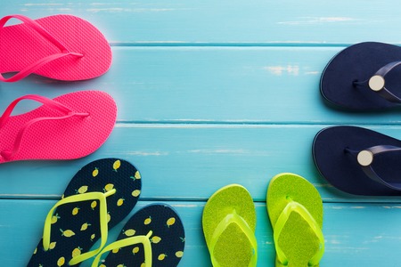 Family vacation background on blue wood, top view with copy space. Beach accessories, flip flops.