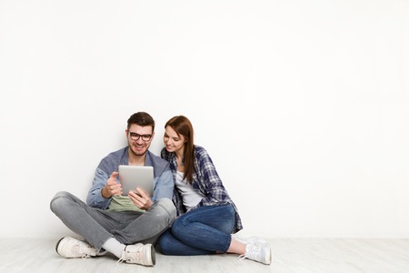 Happy couple with tablet, shopping online, making internet order sitting at home floor in empty living roomの写真素材