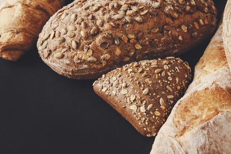 Bakery background, bread assortment on black with copy space. Rye buns, french baguette and...