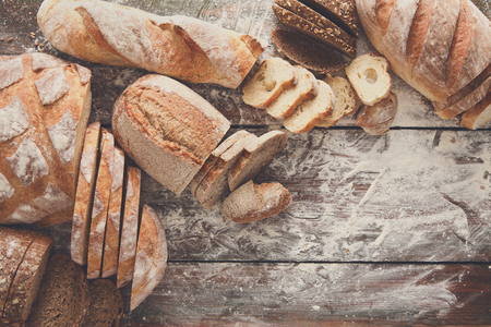 Sliced bread frame on rustic wood background, copy space. Brown and white loaves and flour top view composition with wheat flour sprinkled around.の写真素材