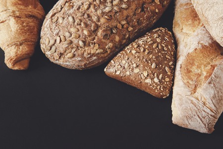 Bakery background, bread assortment isolated on black with copy space. Rye buns, french baguette and...