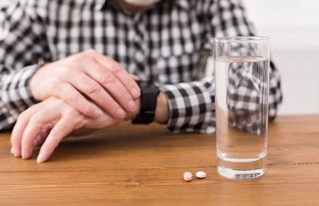 Taking pills. Unrecognizable senior man hands on table with glass of water and medicine. Healthcare, treatment, aging conceptの写真素材
