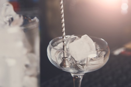Professional bartender in bar mixing ice in glass for drink closeupの写真素材