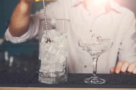 Professional bartender in bar mixing ice in glass for drink closeupの写真素材