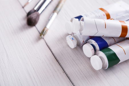 Tools for drawing. Artist paint brushes and oil-paint tubes on white wooden background, copy space, top viewの写真素材
