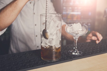 Professional bartender in bar interior mixing cosmopolitan alcohol cocktail, pouring sweet drink into glassの写真素材