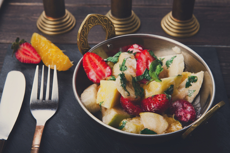Fruit salad with strawberries served in copper bowl on wooden table, top viewの写真素材